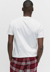 Vit bomulls-t-shirt med korta ärmar och rund halsringning; bärs tillsammans med rödrutiga byxor med ett schackrutigt mönster.