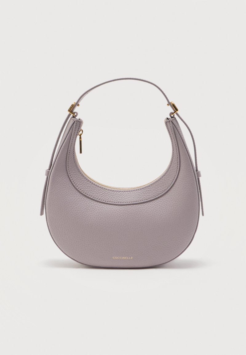 Στρογγυλό δερμάτινο τσαντάκι σε χρώμα λεβάντας με χρυστό φερμουάρ και κοντό λουράκι, με μικρό χρυσό λογότυπο της μάρκας «Coccinelle» στο κάτω κέντρο.