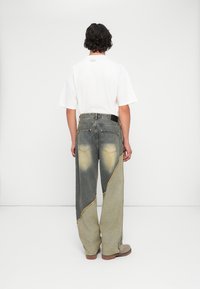 Pantalone širokih nogavica u svijetlom i tamnom denimu s kontrastnim šavovima, sa zigzag uzorkom i stršastim rubovima. Košulja je jednostavna bijela.