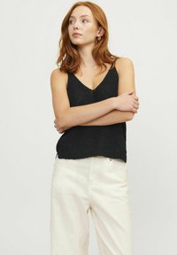 Top de punto negro sin mangas con escote en V, con un corte holgado. Complementado con pantalones de tiro alto en color crema.