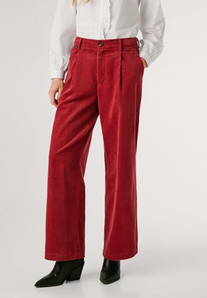Pantaloni larghi in corduroy rosso con texture, pieghe frontali, tasche laterali e chiusura a bottone, abbinati a stivaletti neri con tacco.