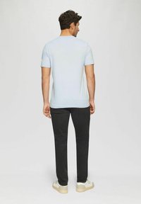 Light blue short-sleeve T-shirt with a round neck, paired with black pants and beige sneakers, viewed from the back. Smooth texture.