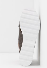 Sandale marron à motifs avec une semelle blanche texturée. Présente un accent en cuir naturel et une marque Michael Kors sur la semelle.