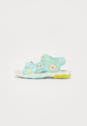 Sandali azzurri chiari con decorazioni floreali, cinturini regolabili e suola bianca con accenti gialli; realizzati in materiali morbidi e flessibili.