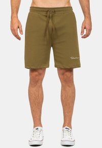 Pantaloni corti verde oliva realizzati in tessuto morbido, con vita elastica e cordino, e un logo bianco sull'orlo. Design casual, alla lunghezza del ginocchio.