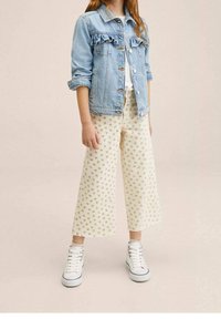 Světlomodrá džínová bunda s volánkovým předním dílem, bílé tričko, krémové široké kalhoty s květinovým potiskem a bílé vysoké tenisky.