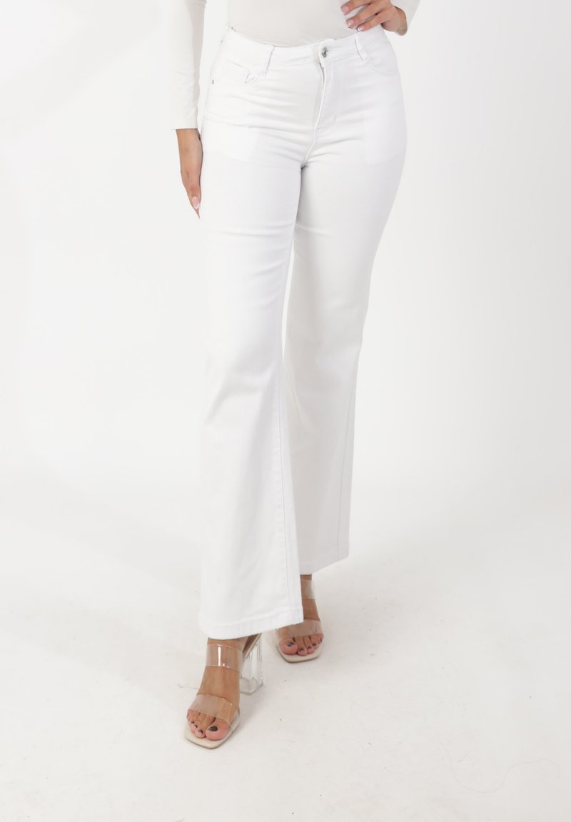 Vita utsvängda jeans med hög midja, slät textur och sidfickor, kombinerade med klara sandaler med blockklack.