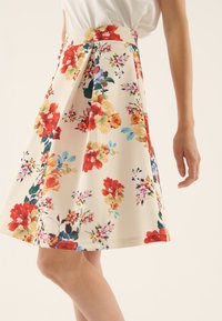 Blommig kjol i lättviktsmaterial, med en krämfärgad bakgrund och röda, rosa och gröna blommor, veckad design och midjeband.