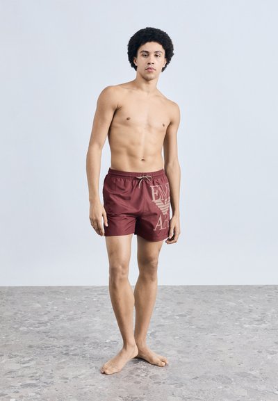 Bordó fürdőnadrág húzózsinóros derékkal, bal oldalon nagy, bézs színű logóval. Simogató, könnyű anyag.