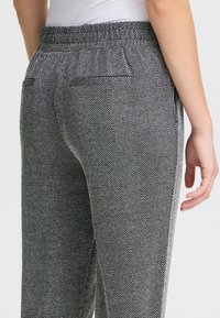 Hosen mit Fischgrätmuster in Schwarz und Weiß, mit einem elastischen Bund und zwei Gesäßtaschen, in einer entspannten, weit geschnittenen Form.