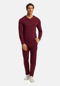 Bordó loungewear set s dlouhým rukávem, V-výstřihem a elastickým pasem, vyrobený z měkkého materiálu, doplněný bílými teniskami.