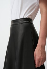 Jupe en cuir noir à taille haute, texture lisse et subtile brillance. Détail de fermeture éclair sur le côté et design évasé s'étendant depuis la taille.