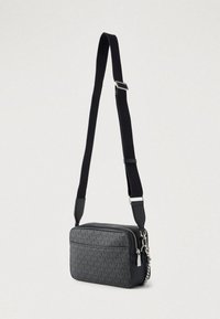 Czarna torebka na ramię z teksturowanym wzorem, zamkiem błyskawicznym, srebrnymi elementami i regulowanym paskiem. Kompaktowy, prostokątny kształt.