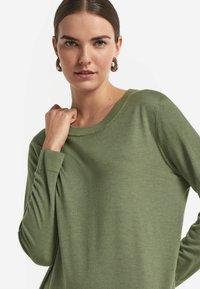 Zielony wełniany sweter z długimi rękawami, prążkowanym dekoltem i mankietami, miękka tekstura, dopasowany krój i subtelne detale szwów.