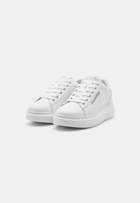 Fehér sneaker, sima szintetikus anyagból készült, fűzős dizájnnal, kerek orral és texturált talppal, minimális márkajelzéssel.