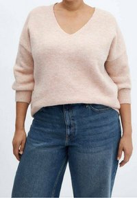 Lichtroze gebreide trui met een V-hals, losse pasvorm en driekwartmouwen, gecombineerd met hoge blauwe jeans. Zachte textuur.