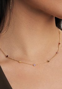 Złoty naszyjnik z łańcuszka, ozdobiony kolorowymi kamieniami szlachetnymi, o delikatnym wzornictwie i równomiernie rozmieszczonych okrągłych kamieniach w różnych kolorach.