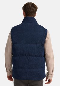 Navyblauer Steppweste mit hohem Kragen, strukturiertem Stoff und horizontaler Steppung. Getragen über einem hellen Langarmshirt.