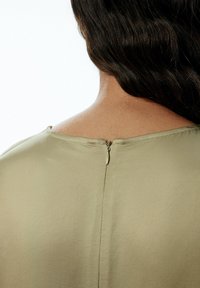 Satin-bluse in olivgrün mit rundem Ausschnitt, mit einem kleinen Reißverschlussverschluss auf der Rückseite und einer glatten, weichen Textur.