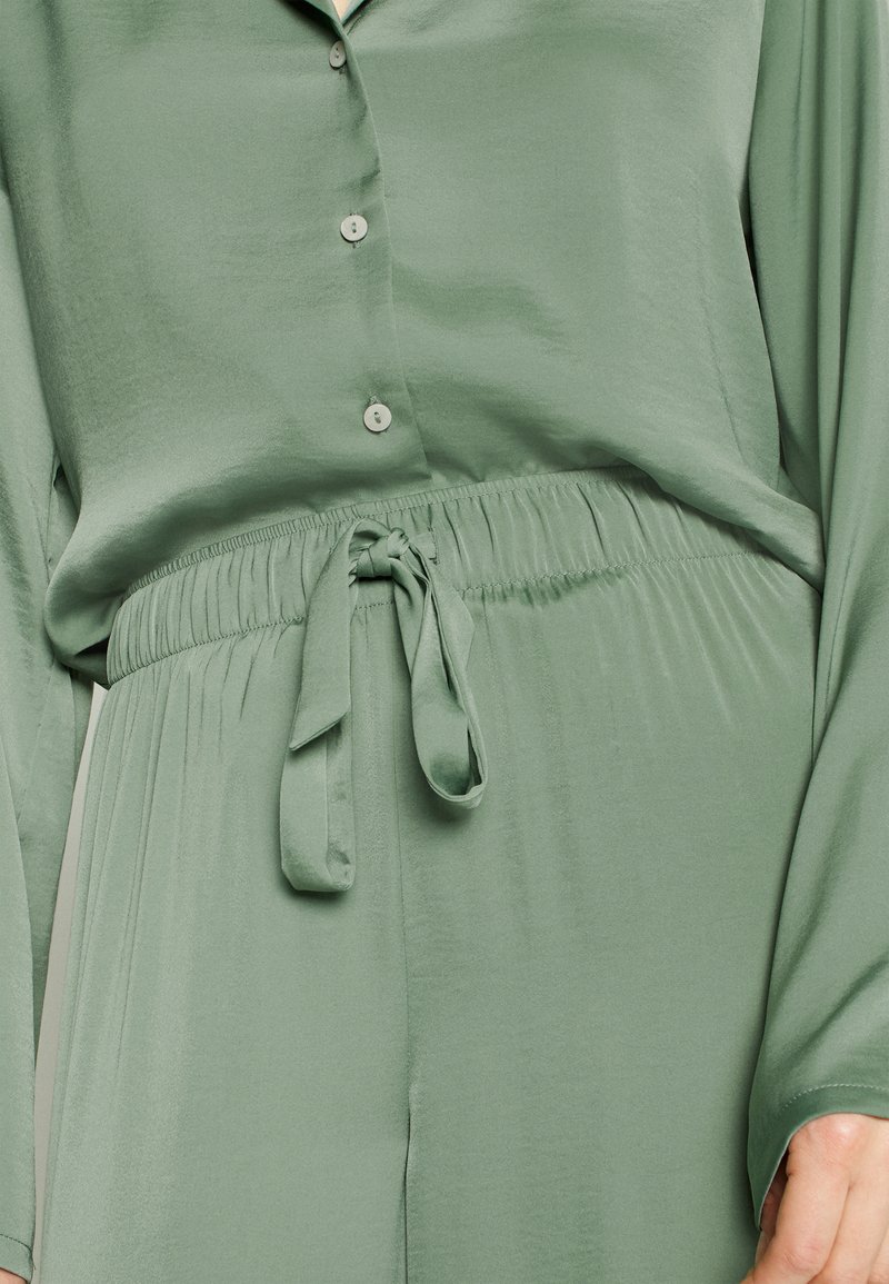 Completo due pezzi verde e setoso caratterizzato da una camicia con bottoni a maniche lunghe e una vita elasticizzata con un dettaglio a fiocco annodato in vita.