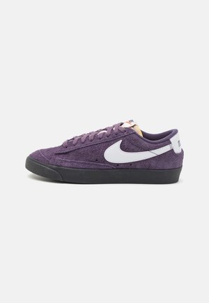 Fialové semišové tenisky s nízkým profilem, bílým logem Nike, černou gumovou podrážkou a kontrastními tkaničkami. Žádné další akcenty.