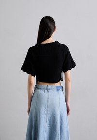 Top corto nero in maglia con design esagonale testurizzato e maniche corte e larghe, abbinato a una gonna in denim blu chiaro con taglio svasato.