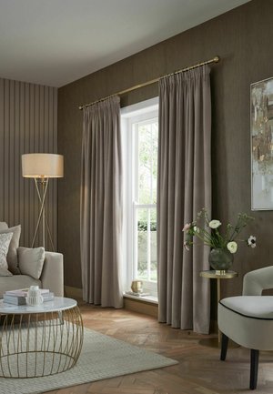 Soft beige curtains framing a window, next to a floor lamp, sofa with cushions, round coffee table, and small side table with a vase of flowers.