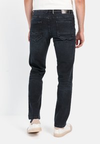 Ciemnoniebieskie, dopasowane jeansy o gładkiej fakturze, z dwiema kieszeniami z tyłu i minimalnym blaknięciem, w połączeniu z białymi trampkami.