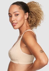 Beige trådlös BH med blommig textur, breda axelband och sömlös design. Slétt tyg och bekv�äm passform accentuerad av delikat sömnad.