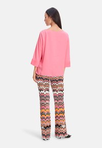 Rosa Baumwolloberteil mit Drei-Viertel-Ärmeln, kombiniert mit mehrfarbigen Zickzack-Musterhosen mit weit ausgestellter Beinpartie.