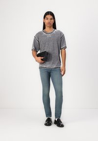 Grå teksturert t-skjorte med rund hals, parret med lyseblå slim-fit jeans og svarte slip-on sko, holder en svart rektangulær veske.