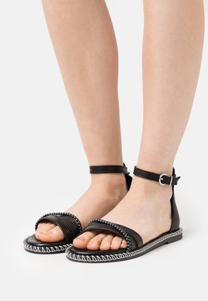 Black leather sandals with an ankle strap, featuring a thick front band, white stitching accents, and a flat sole.