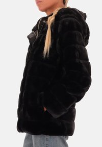 Zwarte nepbont pufferjack met een capuchon, gekenmerkt door een doorgestikte textuur, zijzakken, een ritssluiting aan de voorkant en een ontspannen pasvorm.