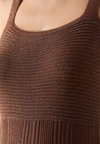 Haut en tricot marron avec nervures fines, agrémenté d'accents scintillants ; bretelles et motif texturé créant une silhouette ajustée.