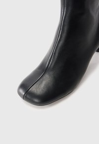 Stivale alla caviglia in pelle nera con punta rotonda, texture liscia e un delicato dettaglio di cucitura lungo il lato. Design aderente con un tacco moderato.