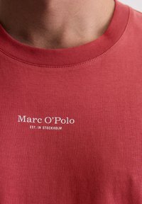 Rode katoenen T-shirt met een ronde hals, voorzien van witte tekst: "Marc O’Polo EST. IN STOCKHOLM" gedrukt op de borst. Gestructureerde stof.