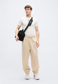 Fitted white athletic shirt, beige jogger pants with elastic cuffs, and a black crossbody bag. White sneakers with dark accents.