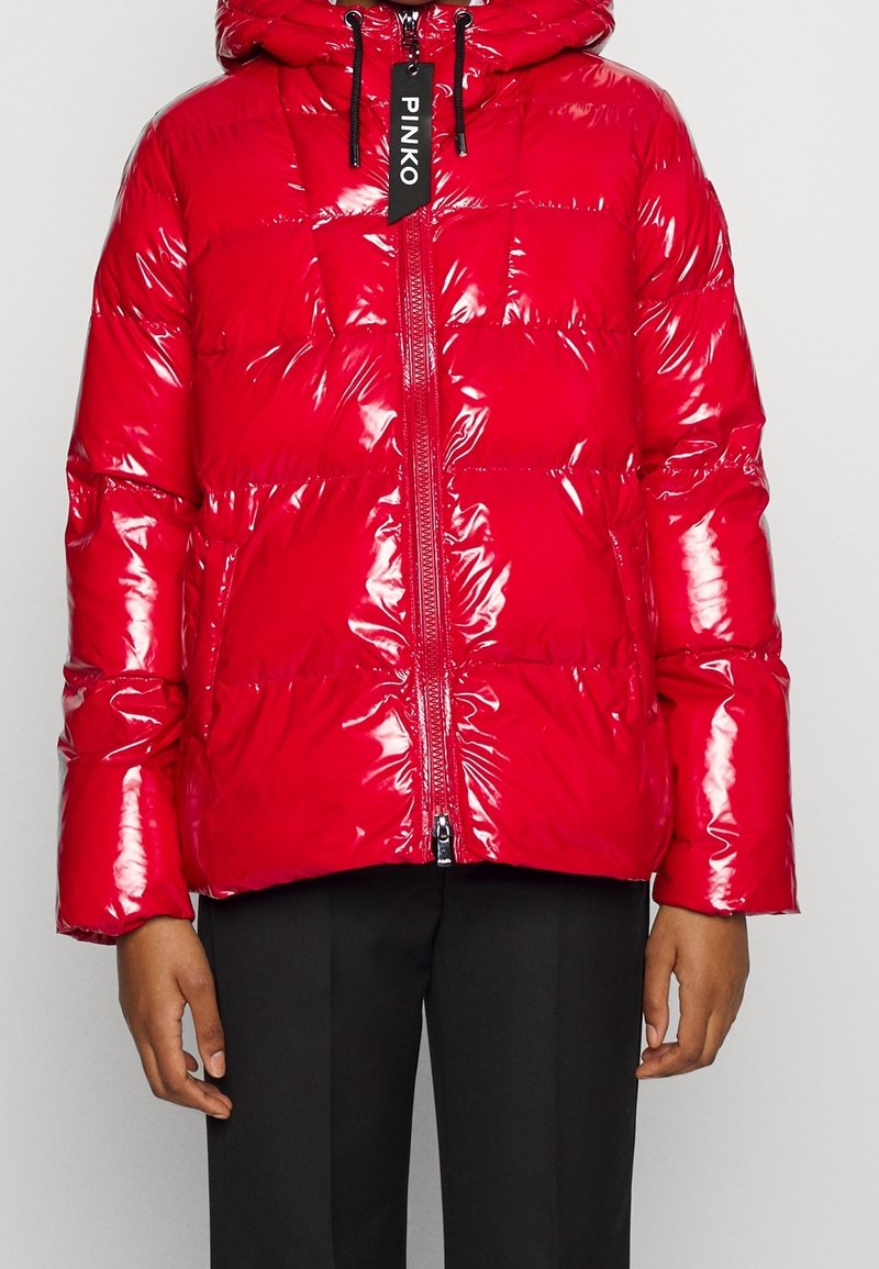 Chaqueta de abrigo roja hecha de material brillante y acolchado, con cremallera frontal, capucha y cordones negros; presenta una etiqueta colgante con "PINKO."