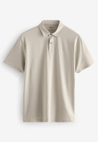 Camisa polo de color beige claro, de manga corta, corte regular, con una tapeta de dos botones y un pequeño logo en el pecho. Textura de tela suave.