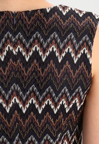 Sømløs beklædning med et zigzag-mønster i marineblå, hvid og rustfarvet. Fremstillet af tekstureret stof med lynlåslukning på ryggen.