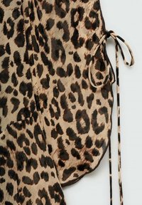 Material cu imprimeu de leopard cu textură moale, având pete negre și maronii pe un fundal bej. Include un detaliu sub formă de cravată neagră pe partea laterală.