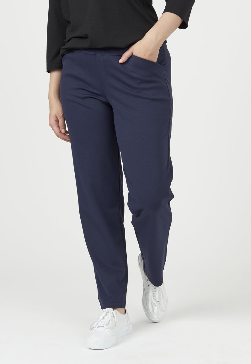 Pantalones stretch azul marino con un diseño ajustado, que presentan bolsillos laterales y una tela suave y transpirable, combinados con zapatillas blancas.