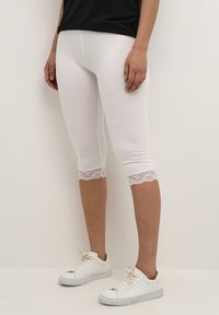 Witte capri-leggings van rekbare katoen, met een kantafwerking aan de zoom, gecombineerd met witte sneakers voor een casual look.