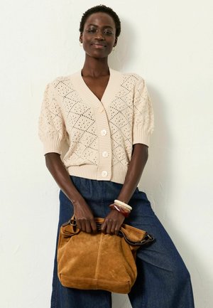 Hellbeige gestrickte Strickjacke mit V-Ausschnitt, kurzen Puffärmeln und Rautenmuster, kombiniert mit dunkler Denim und einer braunen Wildledertasche.