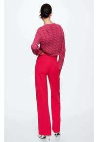 Magenta kabel breiselsweater gecombineerd met felroze wijde broek. De outfit heeft een gestructureerd patroon en een op maat gemaakte, hoge taille.