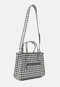 Svartvit rutmönstrad tygväska med korta handtag och avtagbar axelrem. Har en framficka med blixtlås och blank yta.