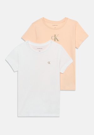 Twee Calvin Klein T-shirts met korte mouwen, één wit met een klein logo, één perzikkleurig met een groot logo, plat neergelegd op een witte achtergrond.
