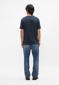 Σακάκι με κοντά μανίκια σε ναυτικό χρώμα, διακοσμημένο με μοτίβο από μικρά, πολύχρωμα λουλούδια, συνδυασμένο με ανοιχτό μπλε φαρδύ παντελόνι τζιν και καφέ παπούτσια.