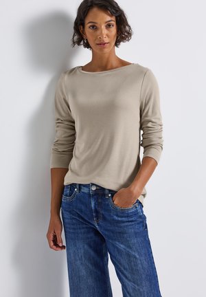 Haut beige à manches longues avec un large décolleté, associé à un jean en denim bleu avec poches et légères distorsions. Texture de tissu lisse.