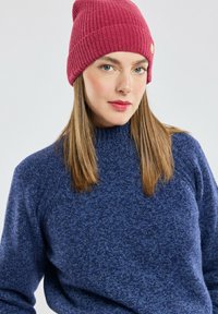 Pull bleu en tricot avec un col montant et un bonnet bordeaux côtelé avec une étiquette. Tissu texturé ; coupe décontractée.
